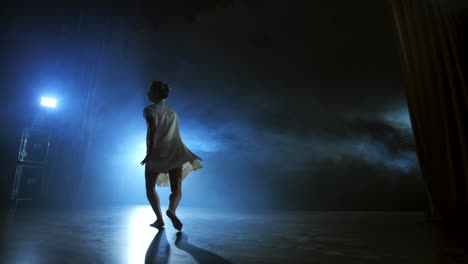 Modern-ballet-dancing-woman-barefoot-doing-spins-and-pirouettes-and-dance-steps-standing-on-stage-in-smoke-in-slow-motion.-Performance-on-stage.